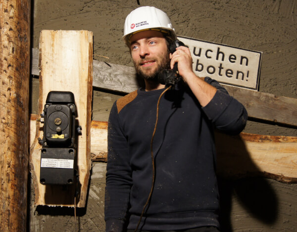 Gamemaster Bergwerk Junger Mann steht im Bergwerk an einem Bergwerkstelefon